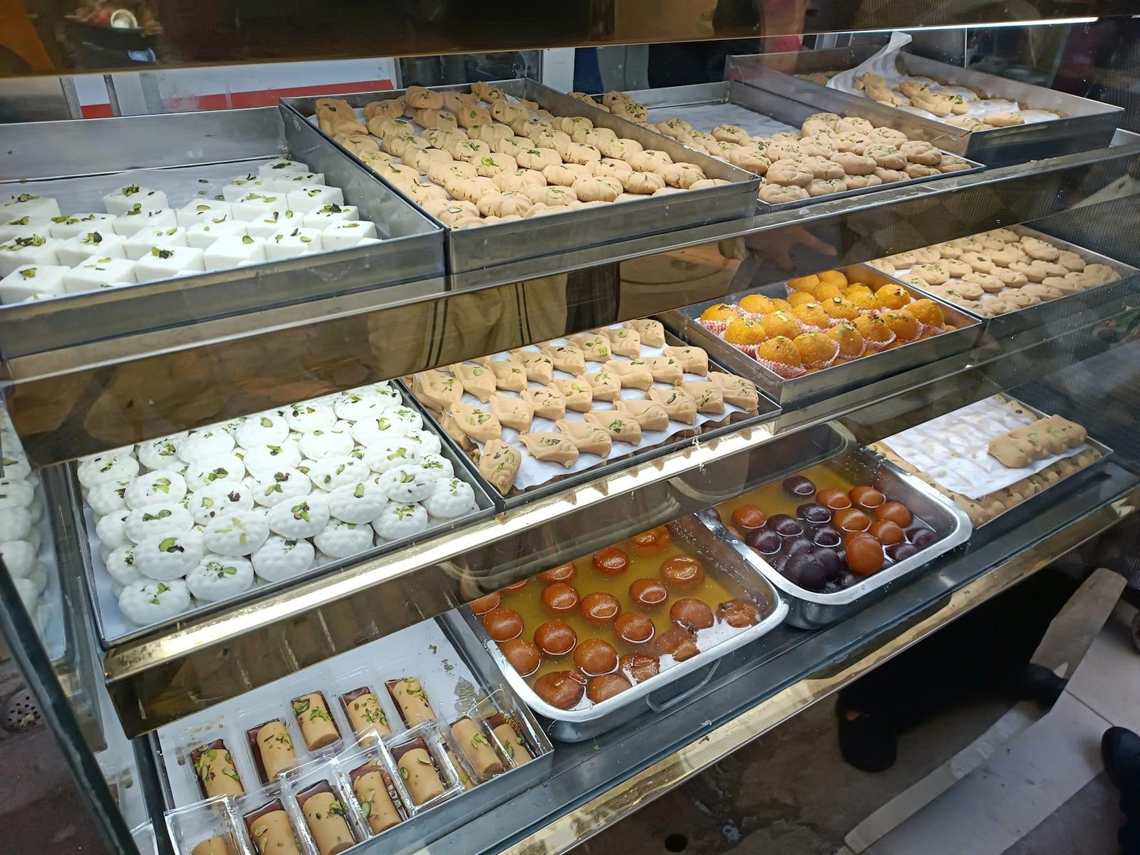 A sweet shop counter lined with trays of fresh mithai